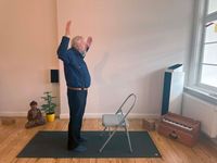 Ein Mann führt eine stehende Yogaübung aus, bei der er sich an einem Klappstuhl abstützt.